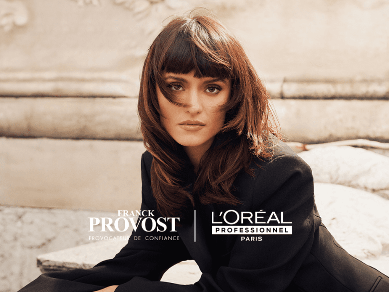 Femme aux cheveux bruns mi-longs avec une frange droite, portant un blazer noir sortant d'un salon Franck Provost après une coloration avec les produits iNOA et Dia color de l'Oréal Professionnel.