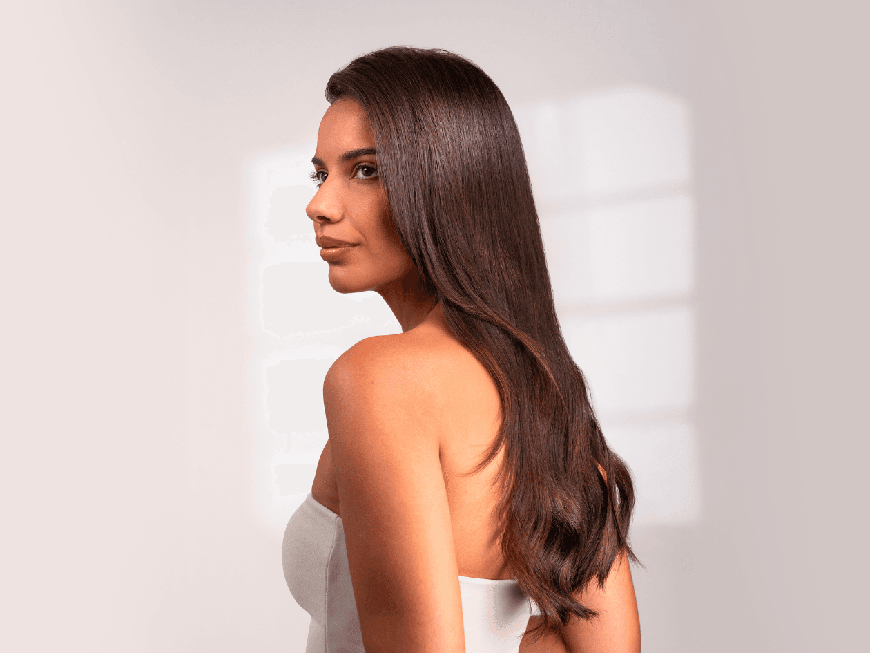 Portrait de profil d'une femme brune aux cheveux longs et ondulés, mettant en avant la brillance, la vitalité et la douceur de sa chevelure suite à un soin Botox capillaire.